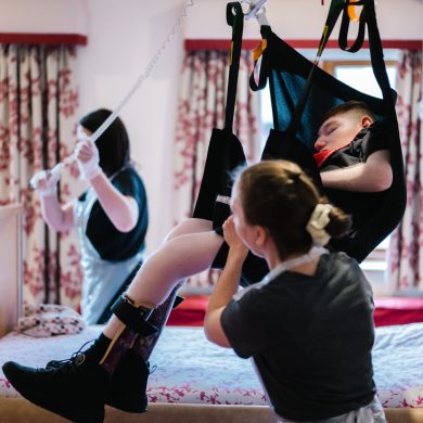 Young person being lifted in a hoist with two nurses