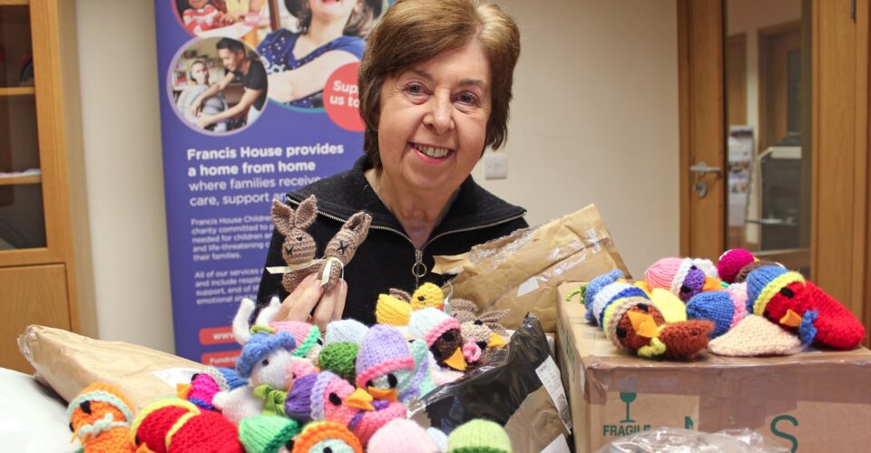 Woman holding knitted bunnies sat in front of parcels of knitted chicks