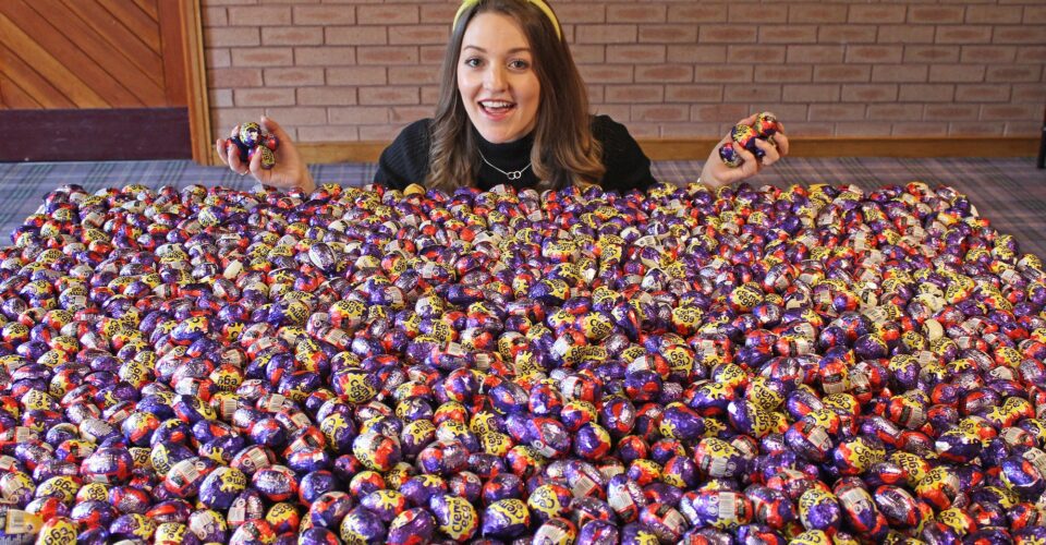 Woman holding chocolate creme eggs kneeling in front of thousands of creme eggs