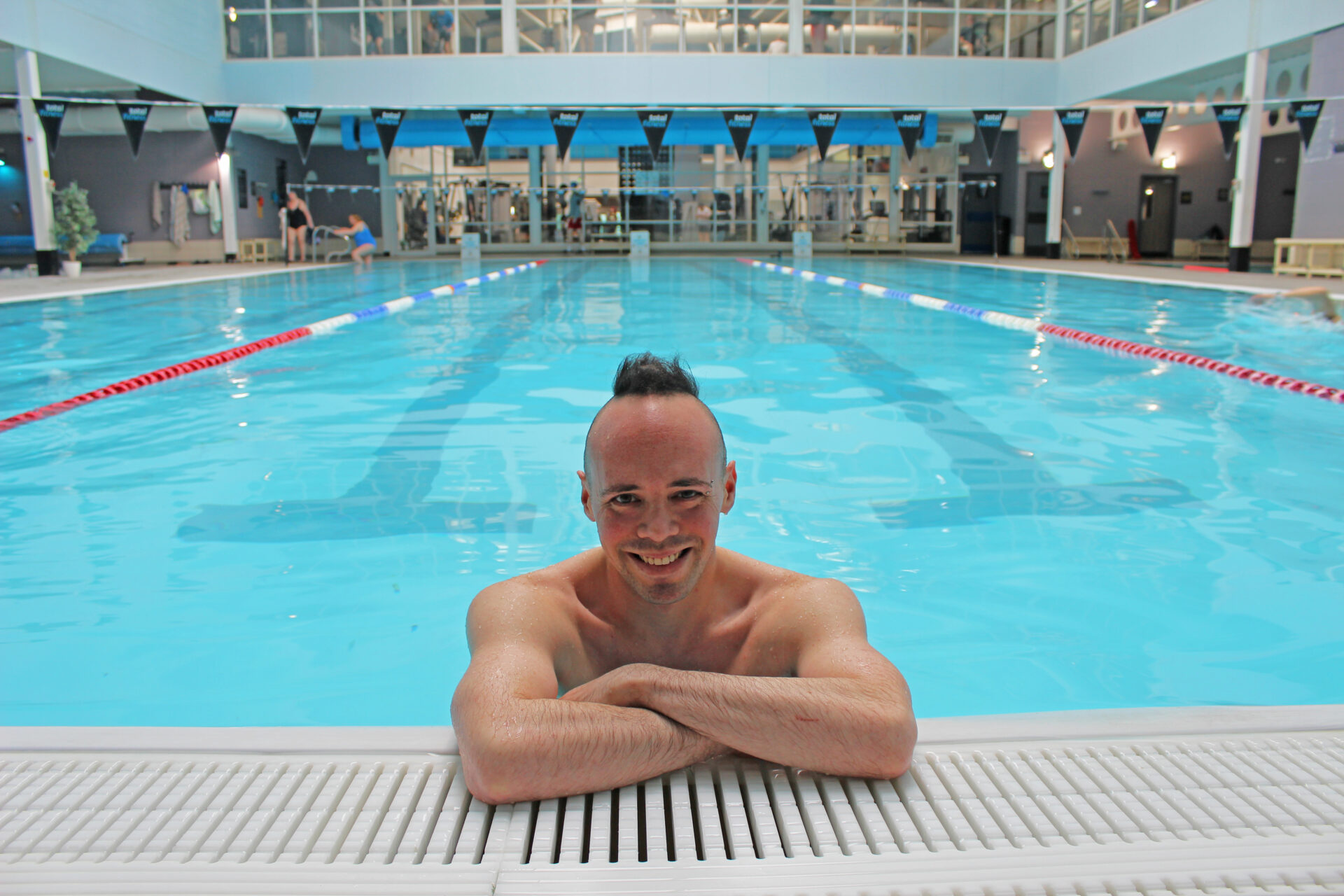 Man in a bright blue swimming pool resting his arms on the pool edge