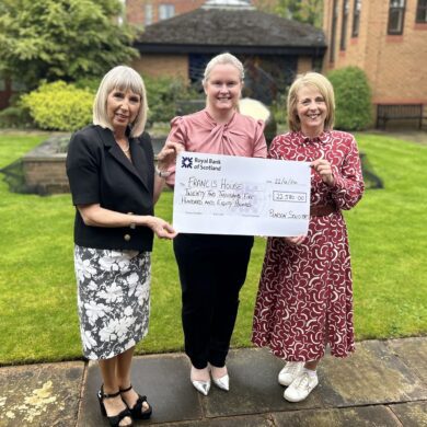 Three women stood in a garden holding a large cheque