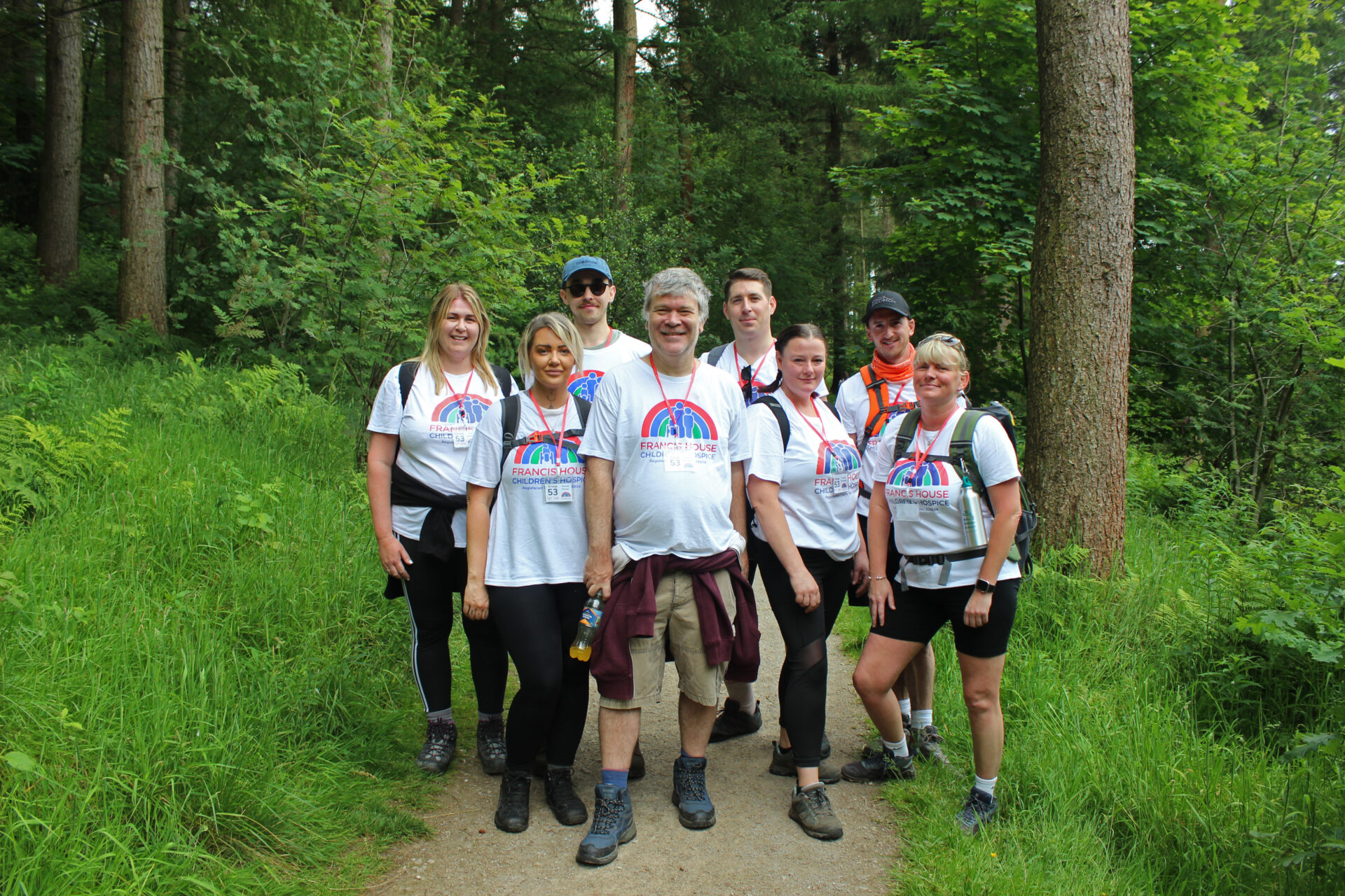 Men and women wearing white t-shirts and hiking boots stood on a forest path