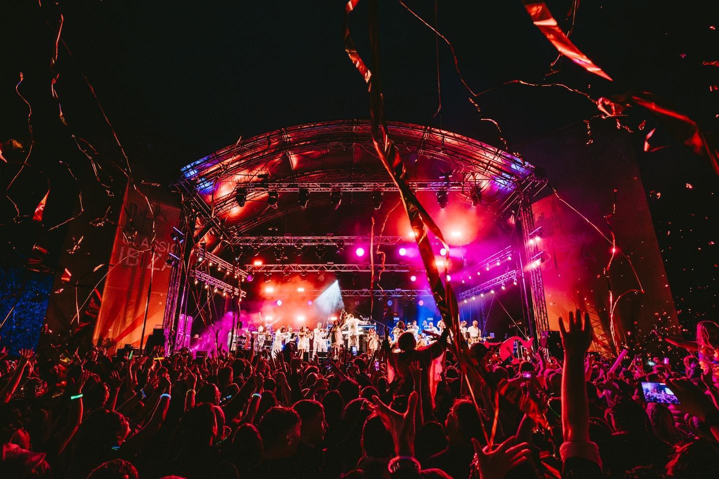 Crowds at a night time concert with stage lit by colourful lighting