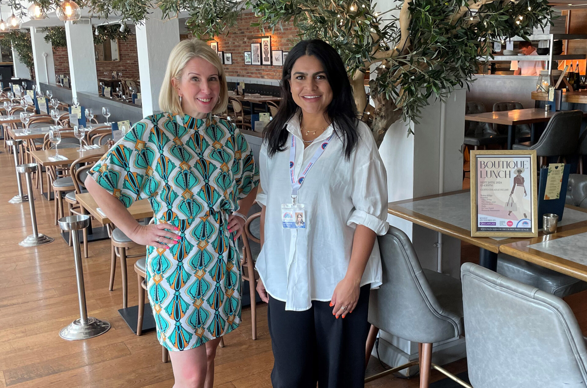 Two women stood in a restaurant in front of tables with an olive tree