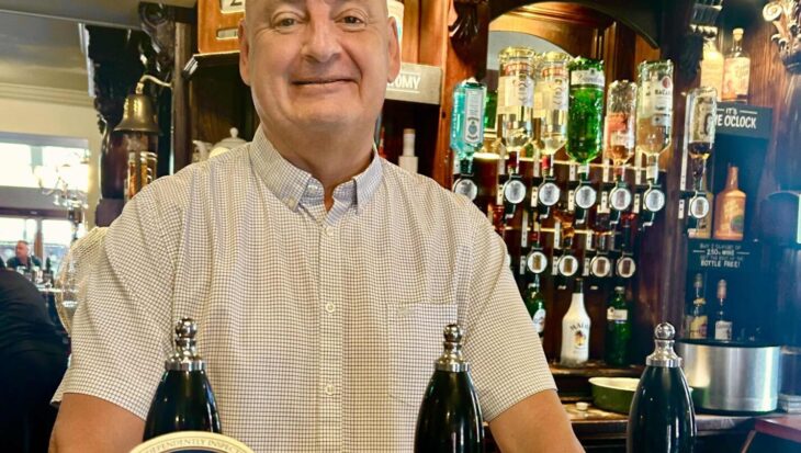 Man stood behind a bar infront of three beer pumps