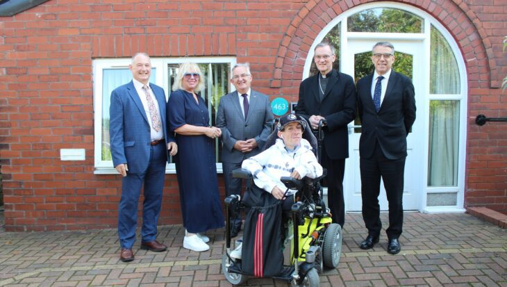 Group of men and women one in a wheelchair in front of a brick house