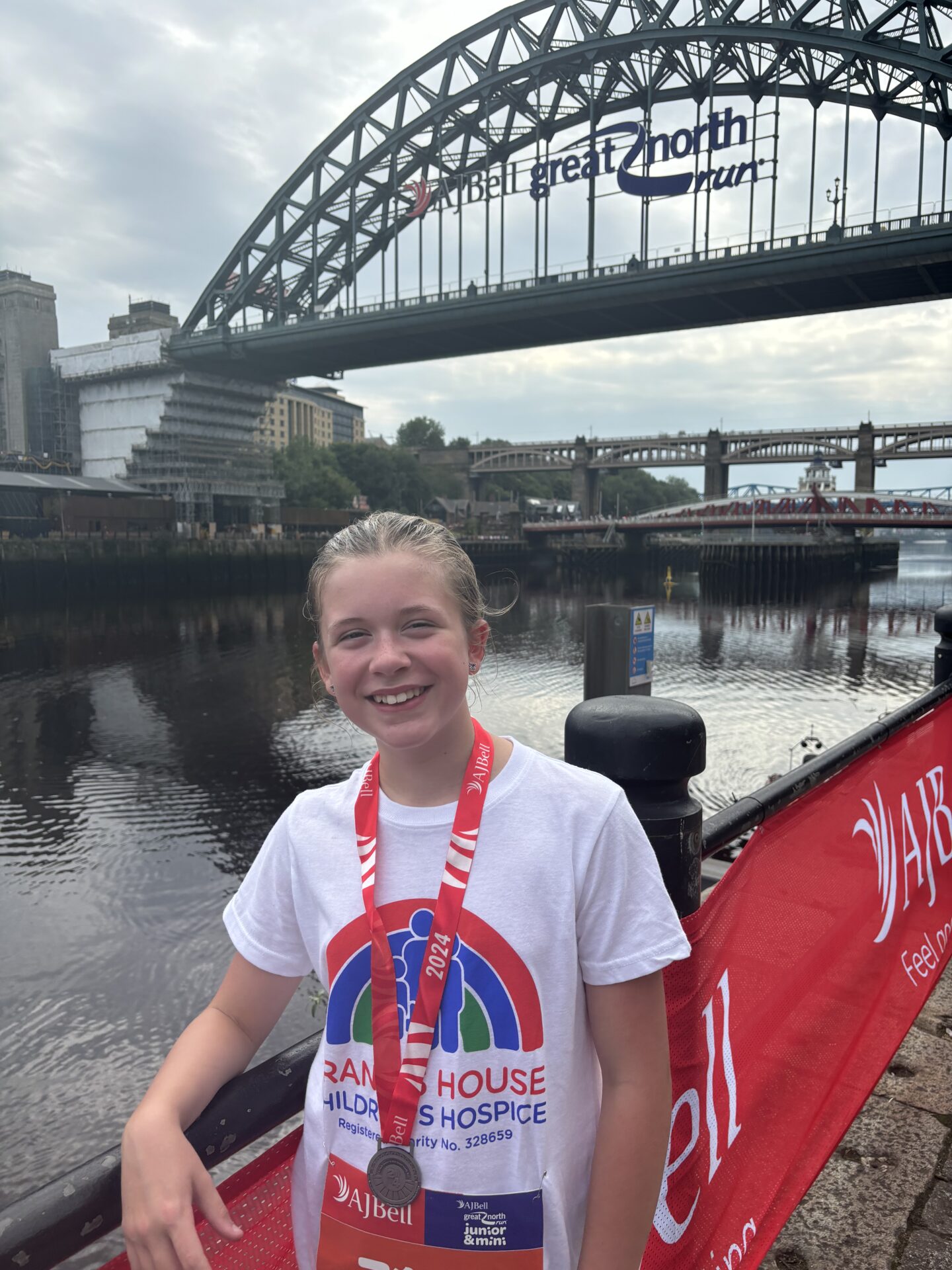 Girl wearing a running t-shirt with a medal around her neck stood in front of the Tyne Bridge