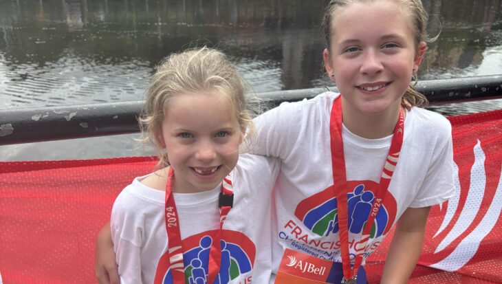 Two girls wearing running t-shirts with medals around their necks sat by the Tyne Bridge