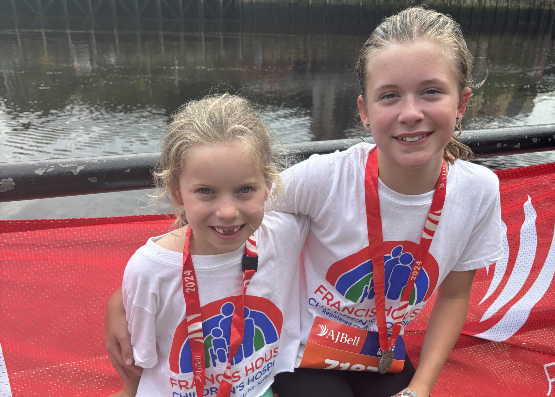 Two girls wearing running t-shirts with medals around their necks sat by the Tyne Bridge