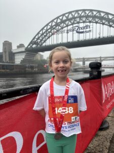 Girl wearing a running t-shirt with a medal around her neck stood in front of the Tyne Bridge