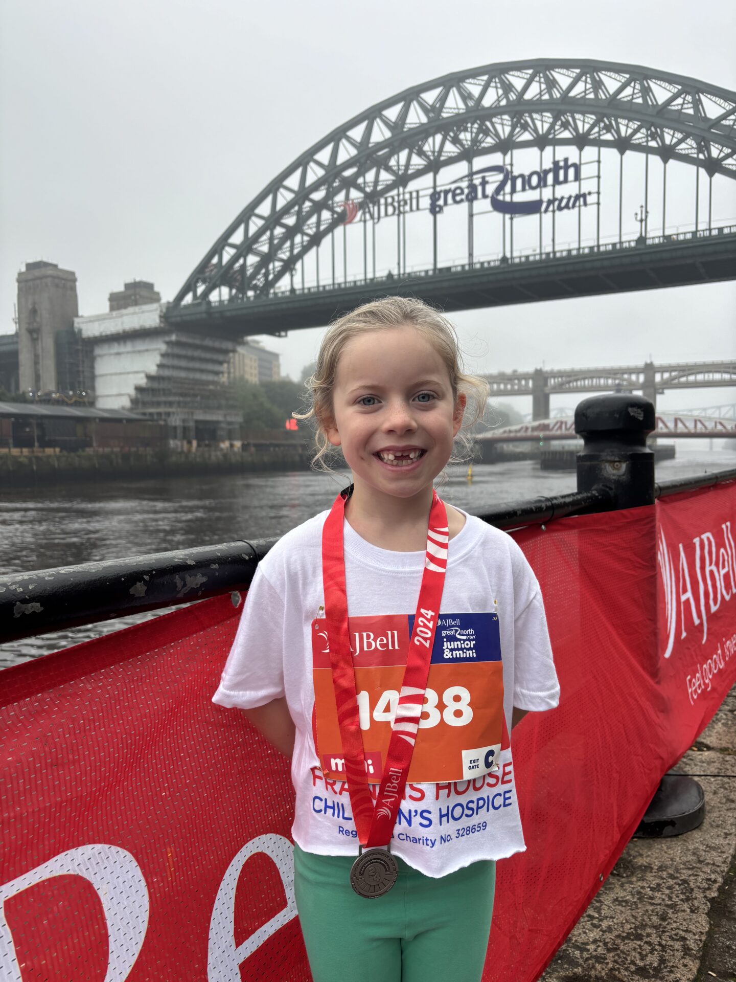 Girl wearing a running t-shirt with a medal around her neck stood in front of the Tyne Bridge