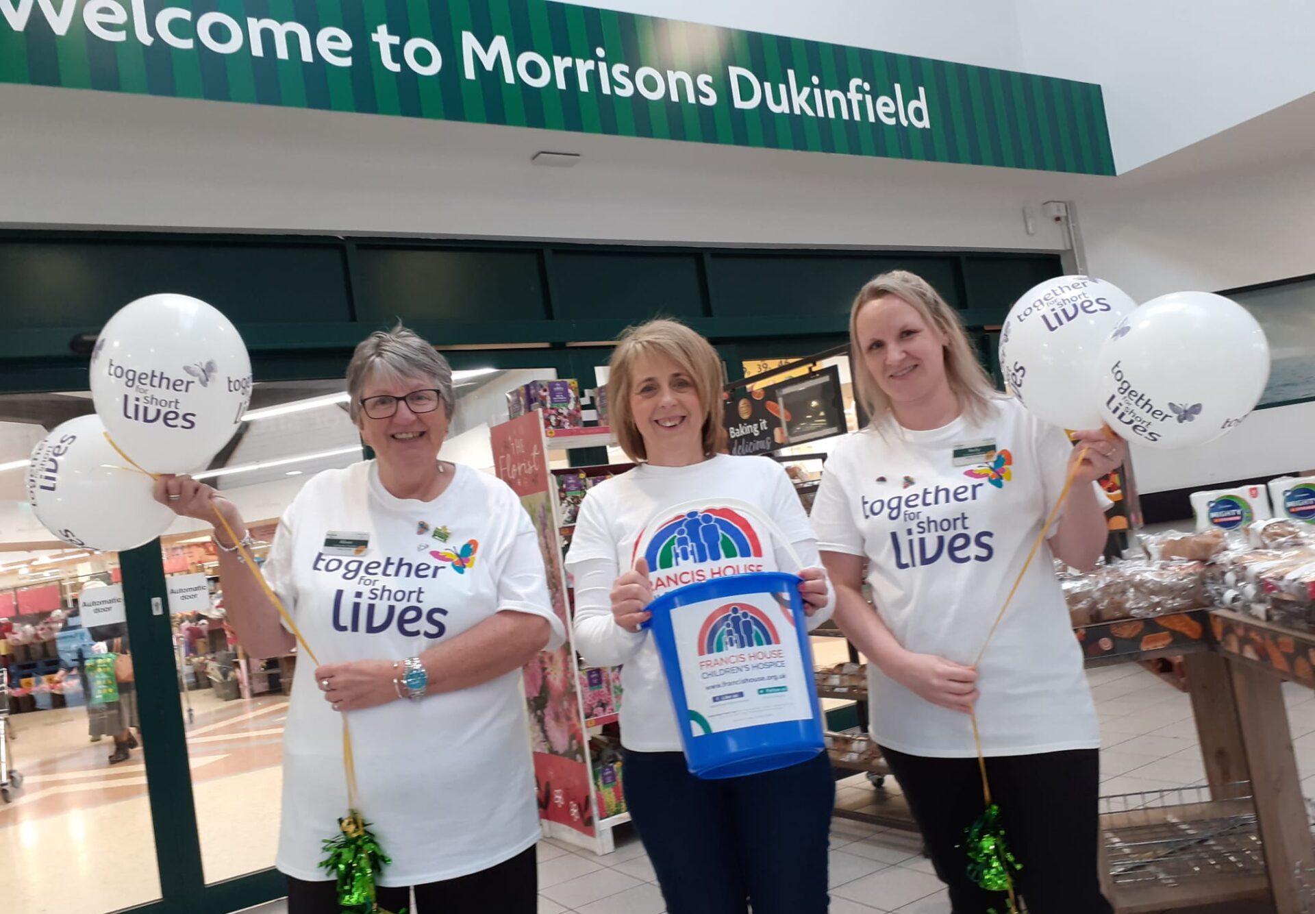 Three women stood outside a Morrisons store holding balloons and bucket