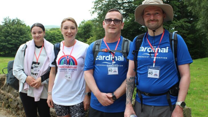 Two women and two men dressed in white and blue t-shirts stood against a stone wall in the countryside